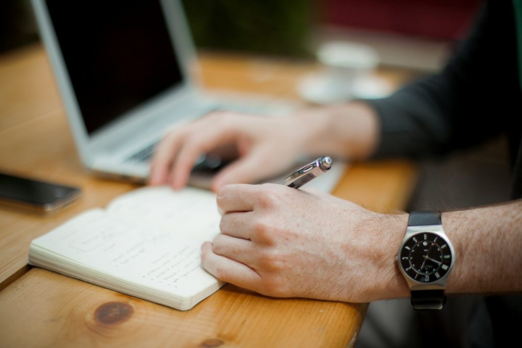 A person at a desk with a computer, surrounded by reference materials on landlord insurance. They are writing and taking notes