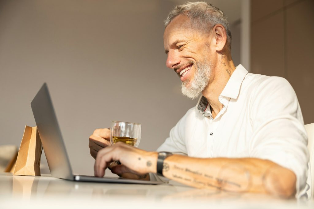 A writer and a laptop with a search engine results page open, surrounded by a stack of books and a notepad with SEO-related notes answering FAQs online