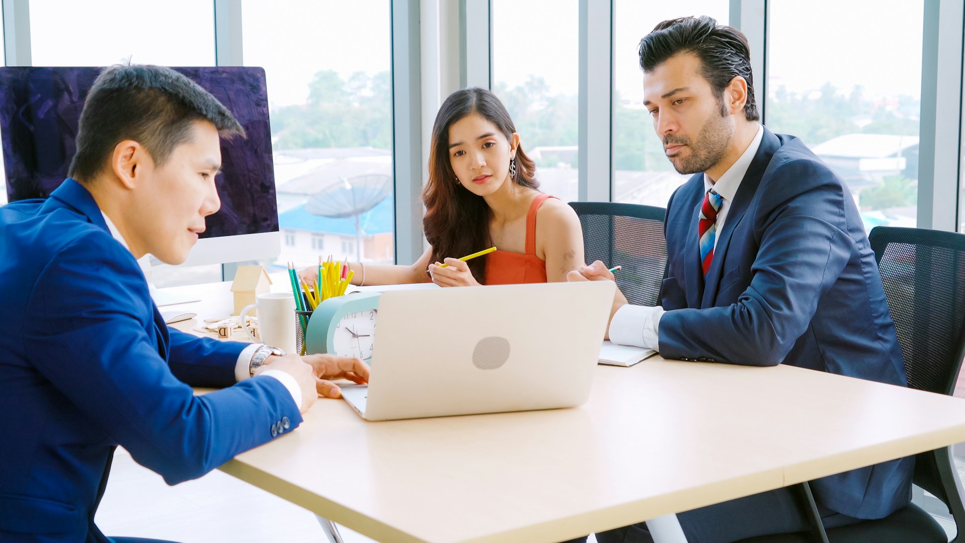 A real estate agent meeting with clients in a modern office, discussing property details and financial information. Blueprints and contracts on the table