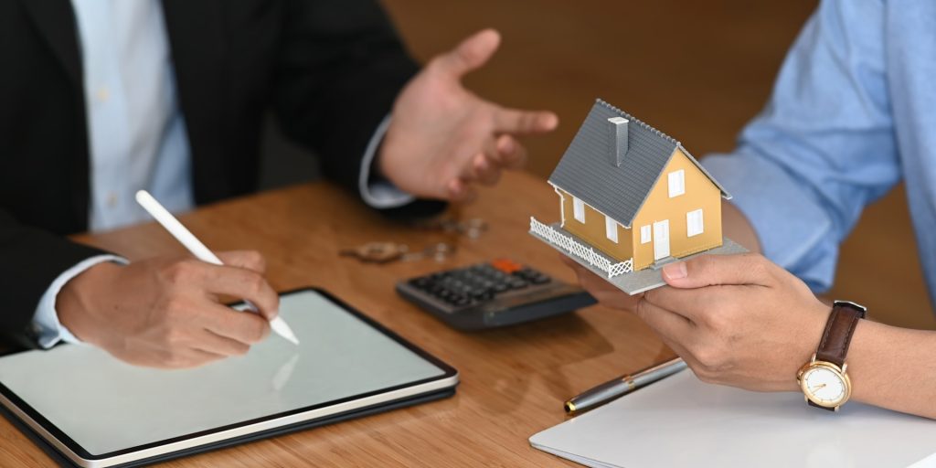 An app creator answering questions about a rental property mobile app to an investor holding a mock-up of a rental property.