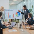 Business professionals in a modern office reviewing charts and graphs around a conference table.